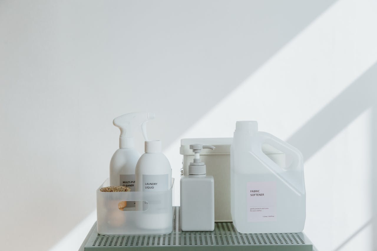 hero-img-01 Clean and simple display of various cleaning products in soft lighting on a white background.