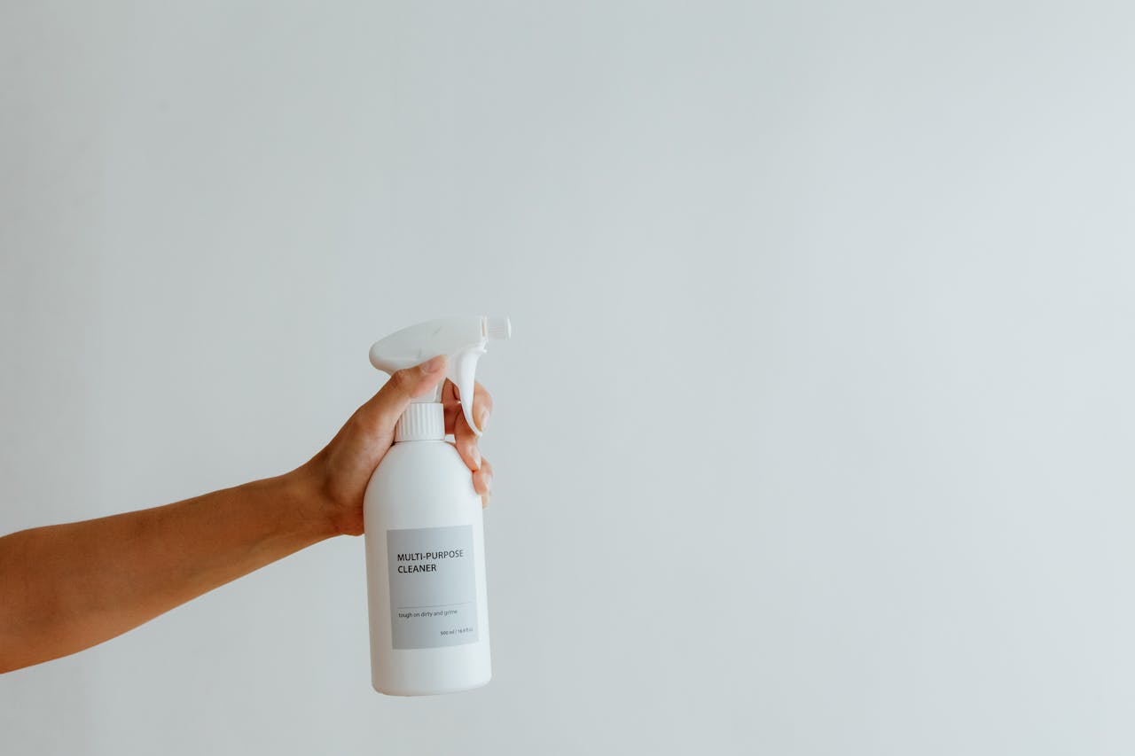 about-01 Close-up of a hand holding a multi-purpose cleaner spray bottle against a white background.